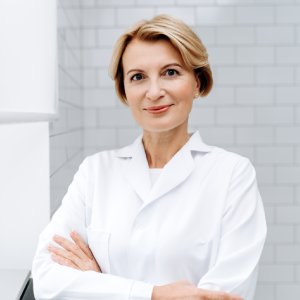Cosmetic dentist in Los Gatos smiling in a modern dental clinic, wearing a white coat with arms crossed.