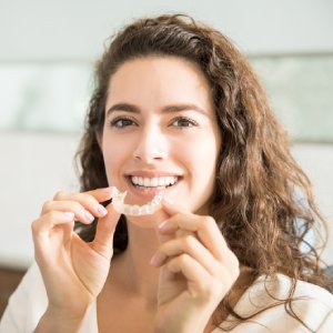 Smiling woman holding clear aligners for invisalign in Los Gatos daily care and a healthy smile.